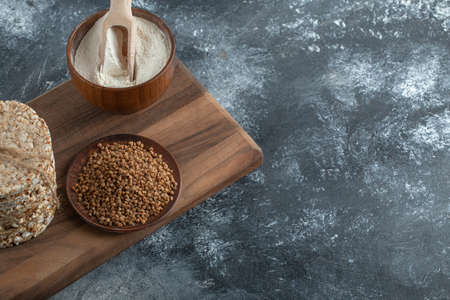 Stack of rice cakes, bowl of flour and buckwheat on wooden boardの写真素材
