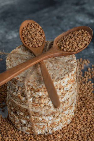Two wooden spoons of raw buckwheat and crispbread on marble surfaceの写真素材