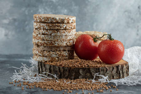 Stack of rice cakes, tomatoes and raw buckwheat on wooden piece