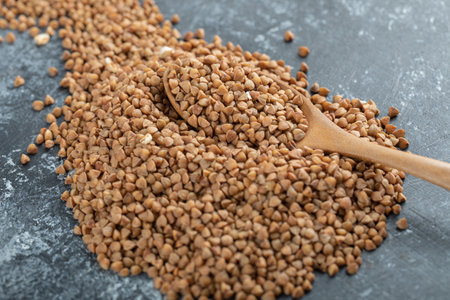 Wooden spoon full of uncooked buckwheat on marble surface