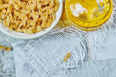 A bowl of uncooked and a bottle of oil on a marble background