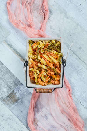 Colorful uncooked pasta on a blue background with pink tablecloth