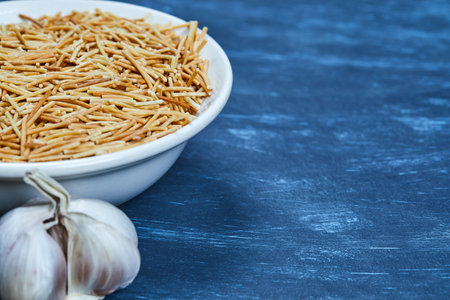 A bowl of dry pasta on blue background with garlicの写真素材