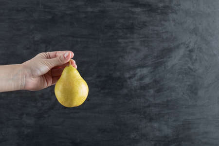 A person holding a yellow pear from the stemの写真素材