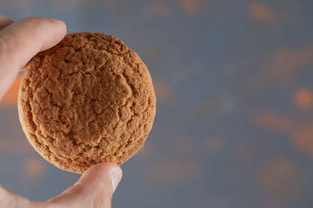 Holding crispy oatmeal cookie between two fingers