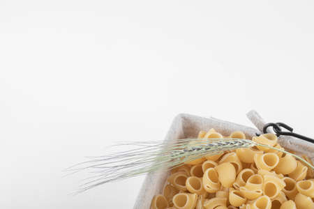 Basket of dry pasta with ear of wheat on white backgroundの写真素材