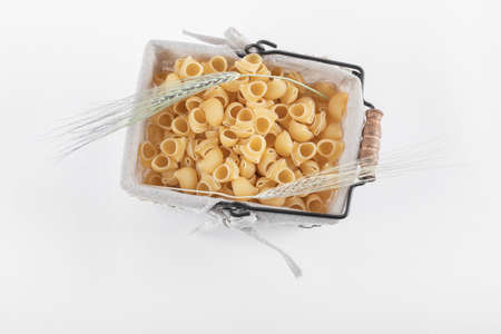 Basket of dry pasta with ears of wheat on white background