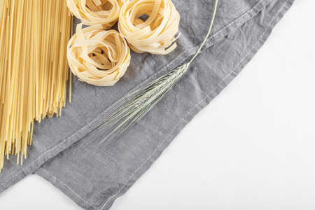 Raw tagliatelle and spaghetti pasta on gray tablecloth