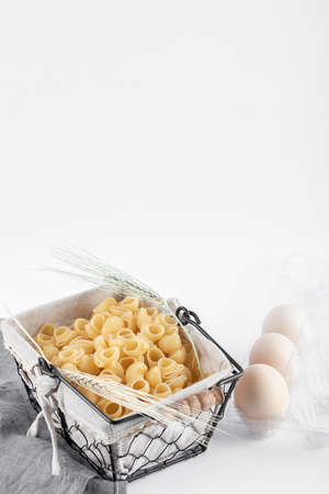 Basket of raw pasta and eggs in container on white surfaceの写真素材