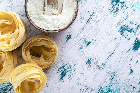 Dry tagliatelle nests and bowl of flour on colorful surfaceの写真素材
