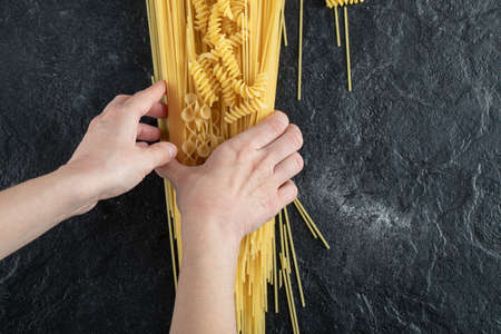 Woman hands holding various pasta on dark surfaceの写真素材