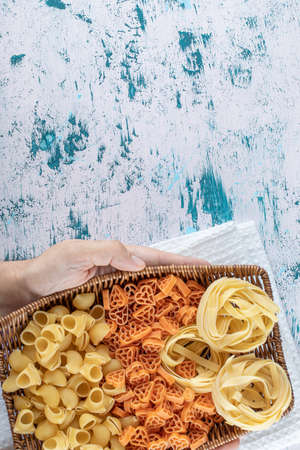 Female hands holding basket of dry pasta on colorful backgroundの写真素材