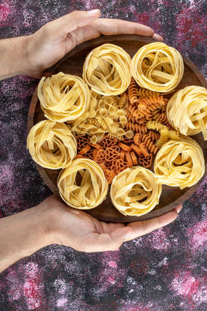 Female hands holding plate of various macaroni on colorful backgroundの写真素材