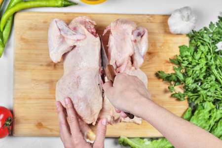 Woman hand cutting raw whole chicken with knife on wooden chopping boardの写真素材