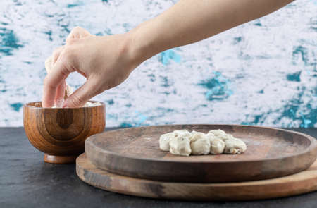 Hand taking a pinch of flour from a wooden bowl on a gray background