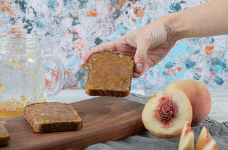 Female hand taking bread slice with jam from wooden cutting boardの写真素材