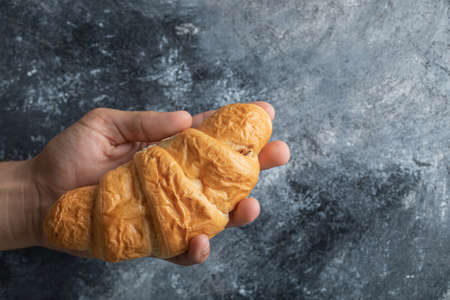 Hand holding a delicious croissant on a gray backgroundの写真素材