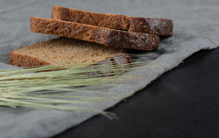Slices of brown bread with wheat on a gray tablelcothの写真素材