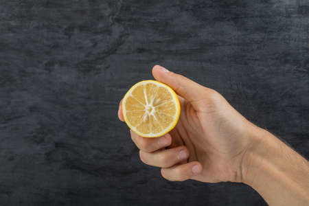 Hand holding a slice of lemon on a dark backgroundの写真素材