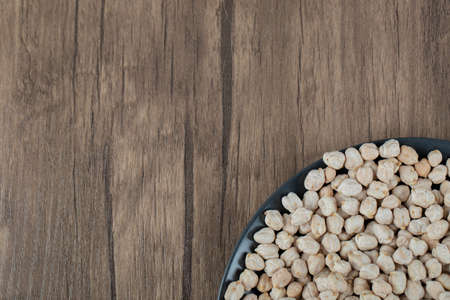 A dark plate full of dried raw white peas on a wooden tableの写真素材