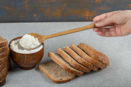 Female hand holding a wooden spoon of flour and slices of bread