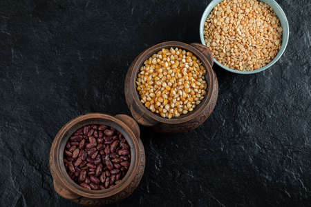 Different kinds of bean seeds, lentil, peas in dishes on a dark background