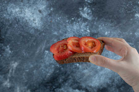 Female hand holding slice of toast with tomatoの写真素材