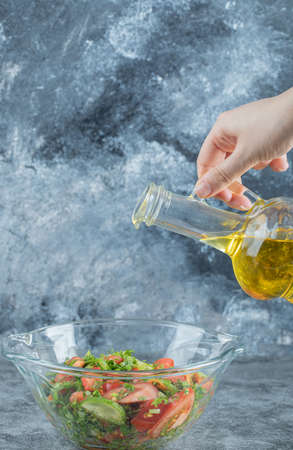 Hand pouring an oil in vegetable saladの写真素材
