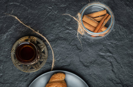 A glass jar full of cinnamon sticks with cup of teaの写真素材