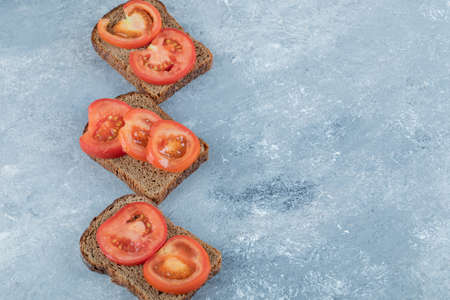 Delicious toasts with slices of tomato on a gray background