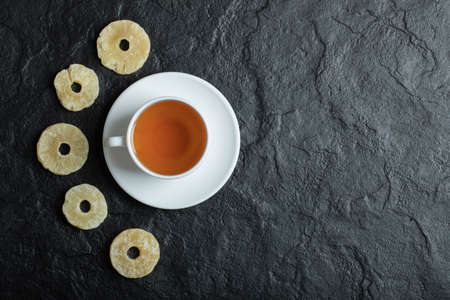 A cup of aroma tea with dried pineapple on a dark backgroundの写真素材