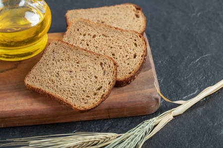 Fresh bread slices on wooden board with spoon of pepper grains