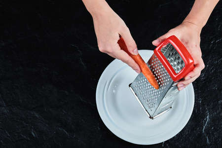 Hand peeling carrot in white plate on the dark background