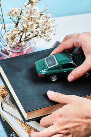 Hand holding a tiny car and books with jar of flowerの写真素材