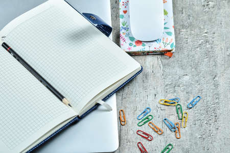 Open notebook, laptop, mouse, clips and a cup of tea on wooden desk
