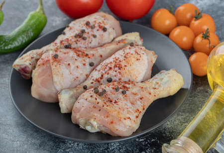 Close up photo raw chicken drumstick on black plate with fresh vegetables.