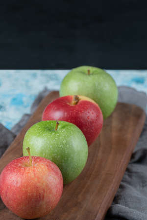 Red and green apples in a row on a wooden board