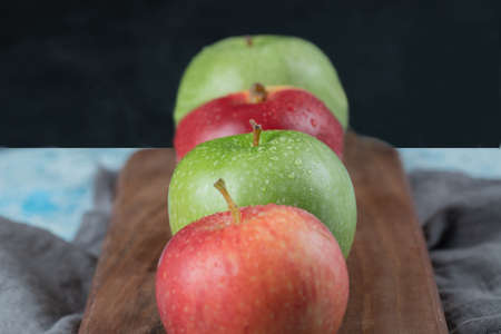 Red and green apples in a row on a wooden boardの写真素材