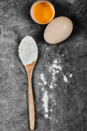 Eggs and wooden spoon of flour on stone tableの写真素材