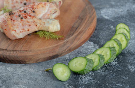 Raw chicken drumstick on wooden board and fresh sliced cucumberの写真素材