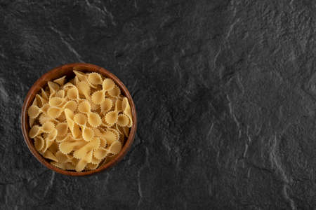 A wooden bowl full of raw farfalle tonde macaroniの写真素材