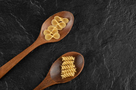 Wooden spoons full of raw girandole and farfalle tonde pastaの写真素材
