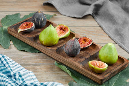 Green and black figs on a wooden platter with leaves and tablecloth