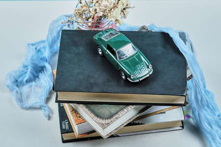 A tiny car on the top of books with jar of flowers