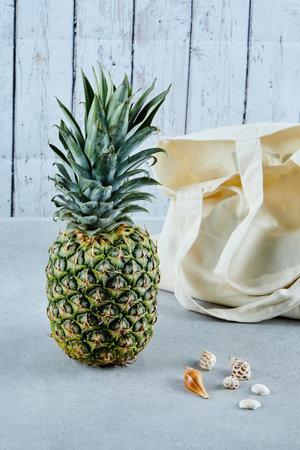 Ripe pineapple and white bag on blue background with seashells