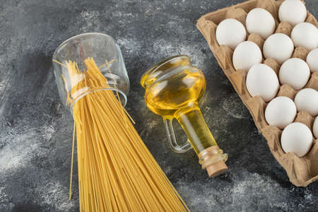 Raw dry spaghetti with uncooked eggs and a bottle of oil