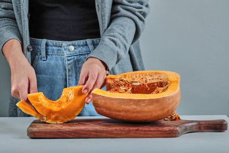 A woman hand cutting a slice of pumpkin with knife on the wooden boardの写真素材
