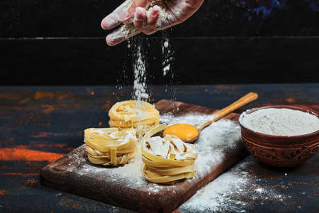 Hand pouring powder into raw tagliatelle pasta on wooden boardの写真素材