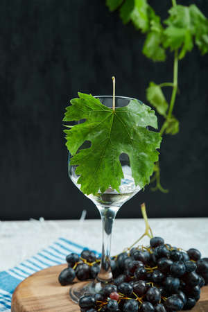 A plate of black grapes and a glass of wine with leaf on dark backgroundの写真素材