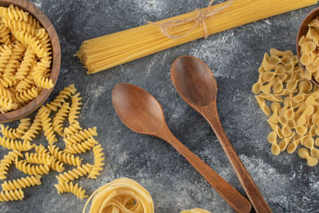 Various types of uncooked pasta with wooden spoonsの写真素材